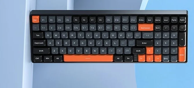 The AULA S100 on a light desk: the tight 98% layout with orange Esc, Backspace, spacebar and arrows