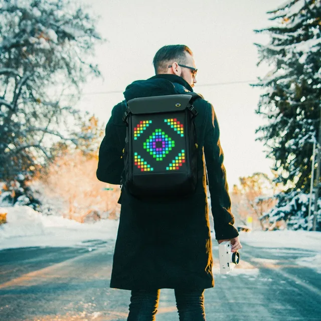 Мужчина на зимней улице с чёрным рюкзаком Pixoo Backpack-M, на экране светится пиксельный узор