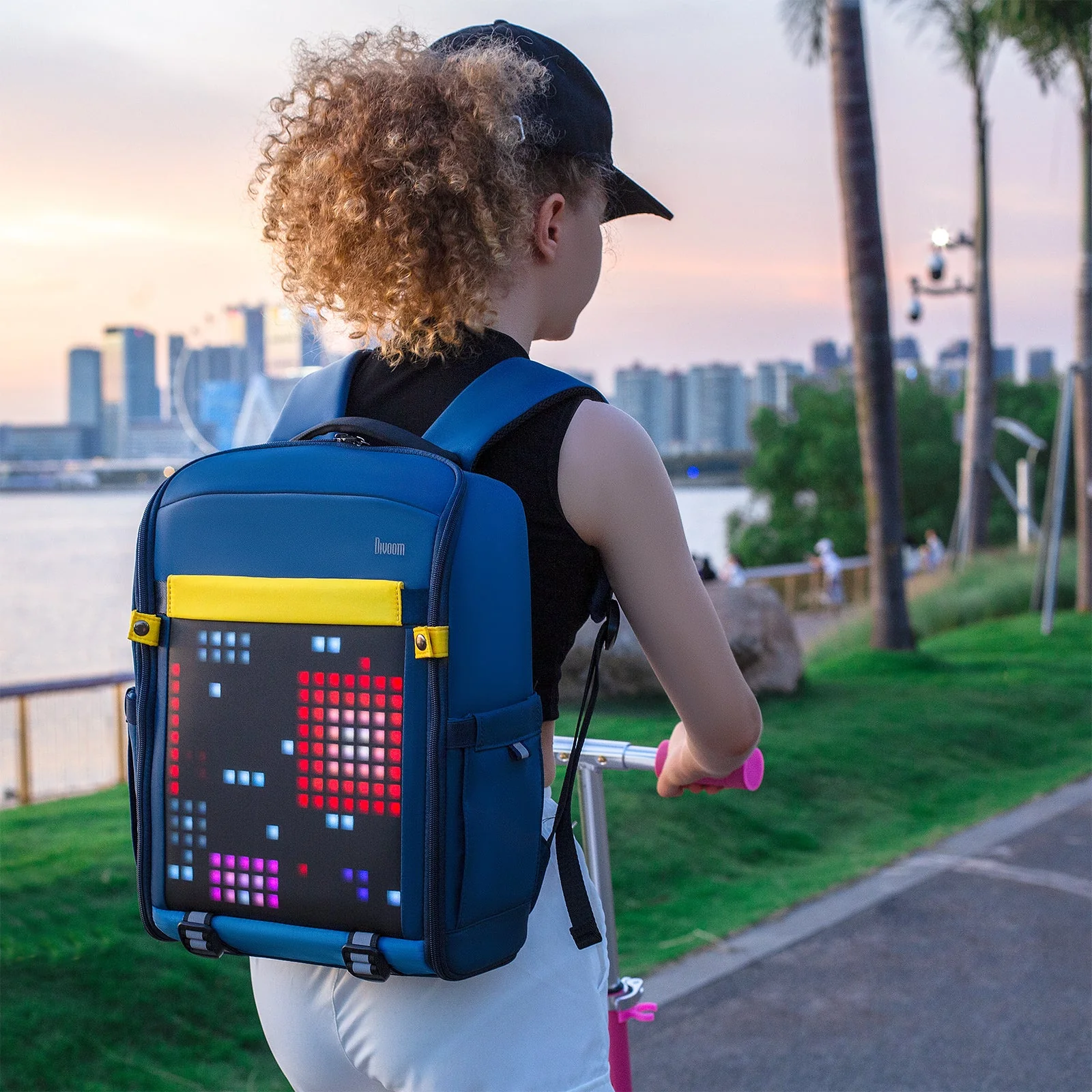 Подросток на самокате у набережной с рюкзаком Divoom Backpack-S, пиксельный рисунок светится в сумерках