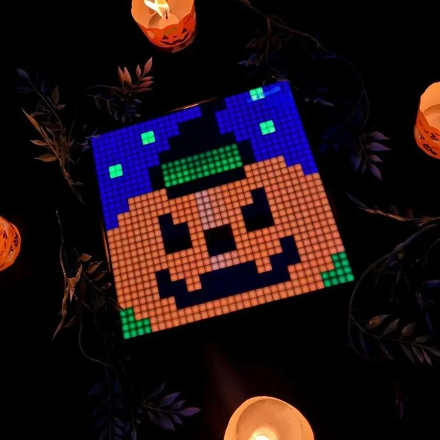 Divoom Pixoo-Max в тёмной комнате со свечами, на экране пиксельная тыква